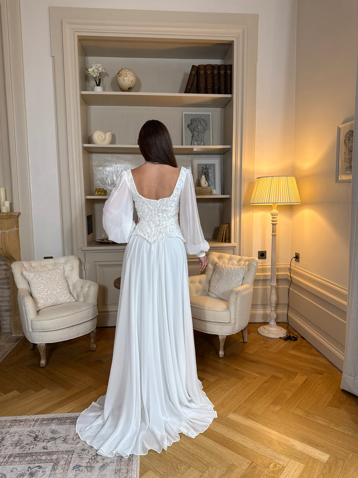 Longue robe de mariée blanche élégante à manches longues, col carré et coupe fluide sans fente. Une robe raffinée pour un mariage chic.