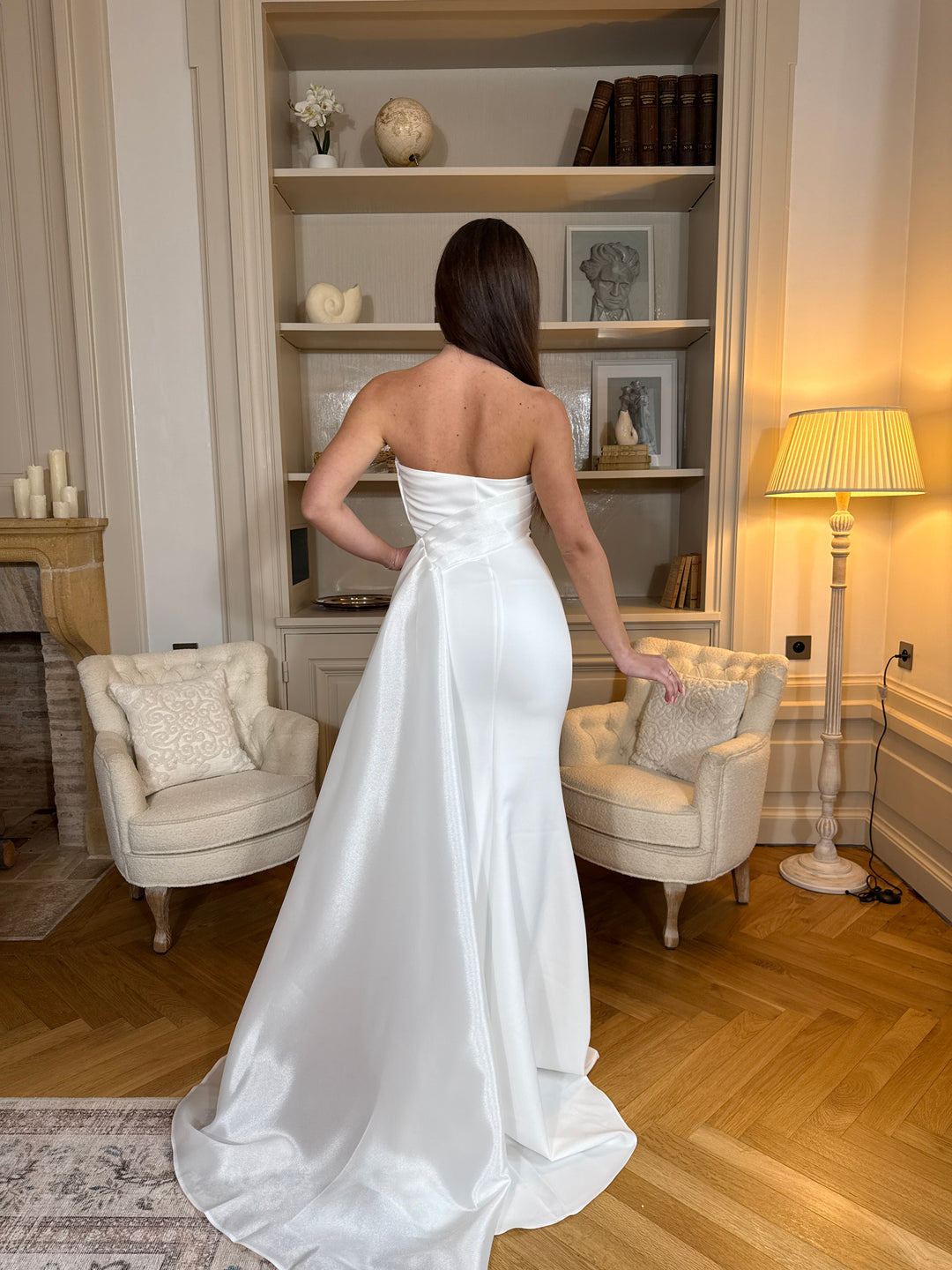 Longue robe de mariée blanche élégante, col bustier sans manches, coupe fluide sans fente. Une robe raffinée pour un mariage chic et intemporel.