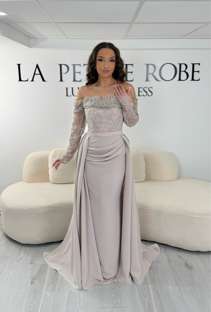 Robe de soirée beige longue avec dentelle, décolleté épaules dénudées et traîne amovible. Élégante, sans fente, idéale mariage 2026.