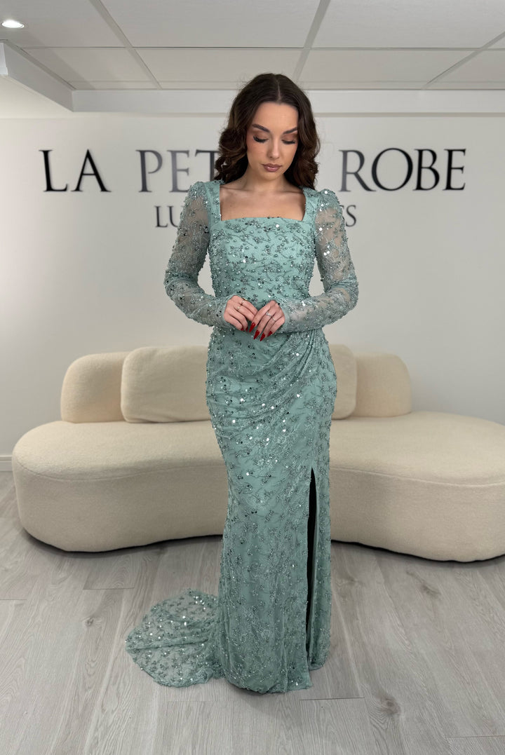 Robe de soirée vert d’eau élégante avec col carré, manches longues et fente glamour. Idéale pour un look chic, lumineux et raffiné.