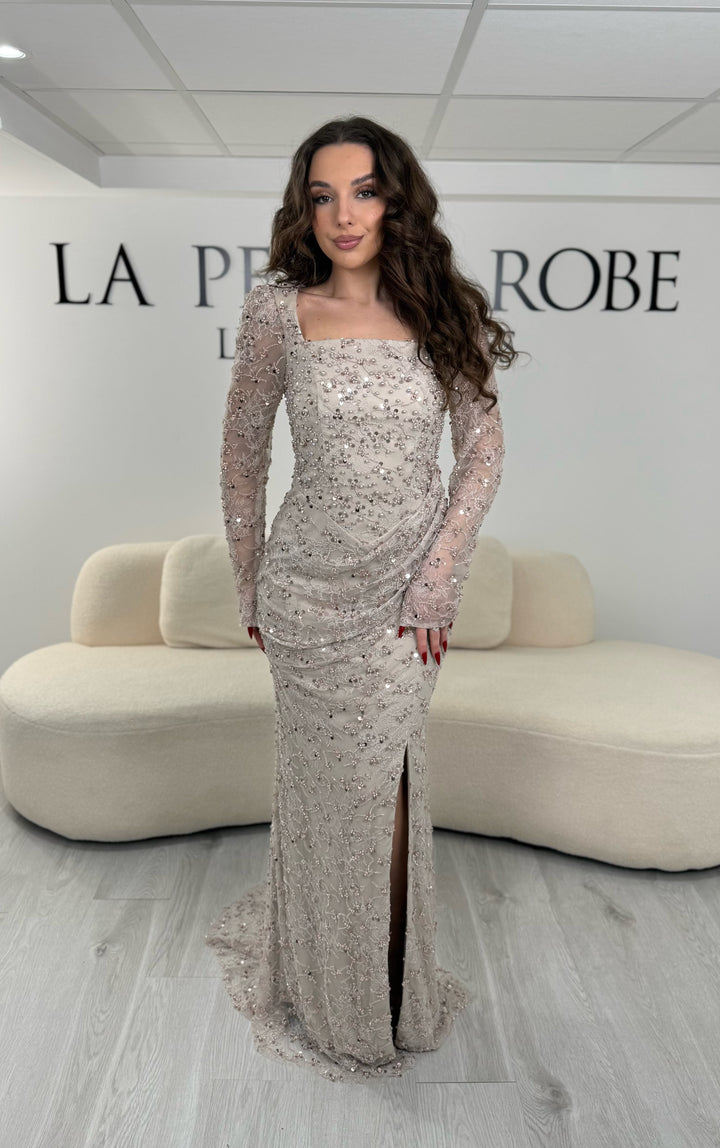 Robe de soirée taupe élégante avec col carré, manches longues et fente glamour. Idéale pour un look chic, lumineux et raffiné.
