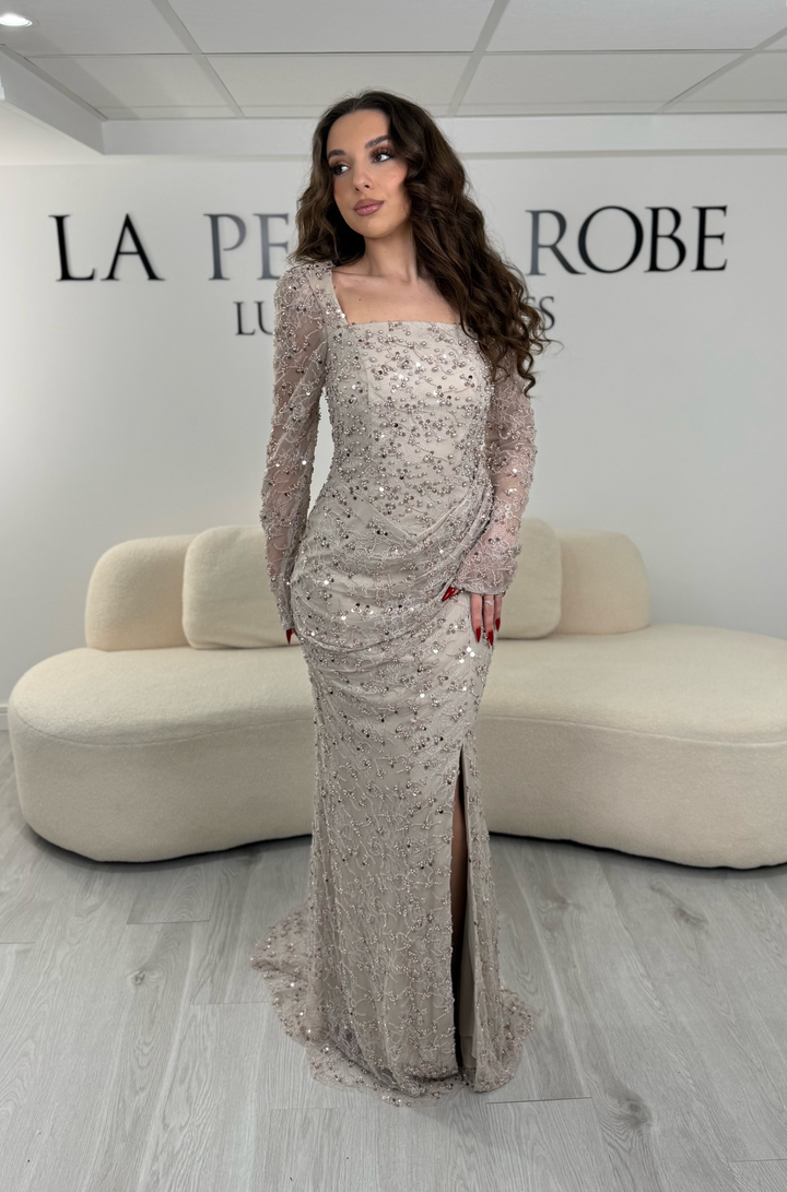 Robe de soirée taupe élégante avec col carré, manches longues et fente glamour. Idéale pour un look chic, lumineux et raffiné.