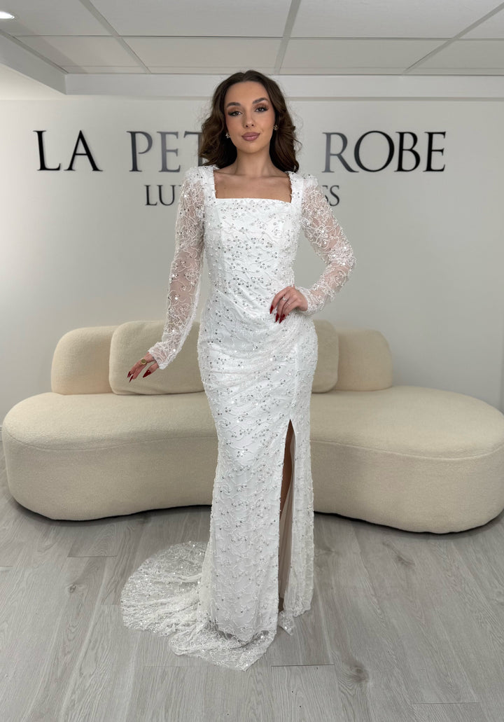 Robe de mariée blanche élégante avec col carré, manches longues et fente glamour. Idéale pour un look chic, lumineux et raffiné.