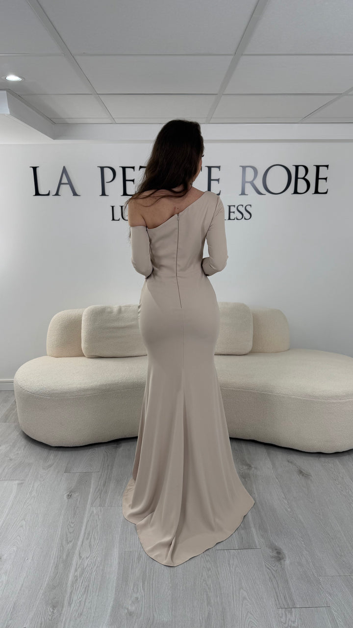 Robe de soirée beige avec col asymétrique et manches longues. Coupe ajustée avec fente sur le côté, idéale pour une allure élégante et sophistiquée.