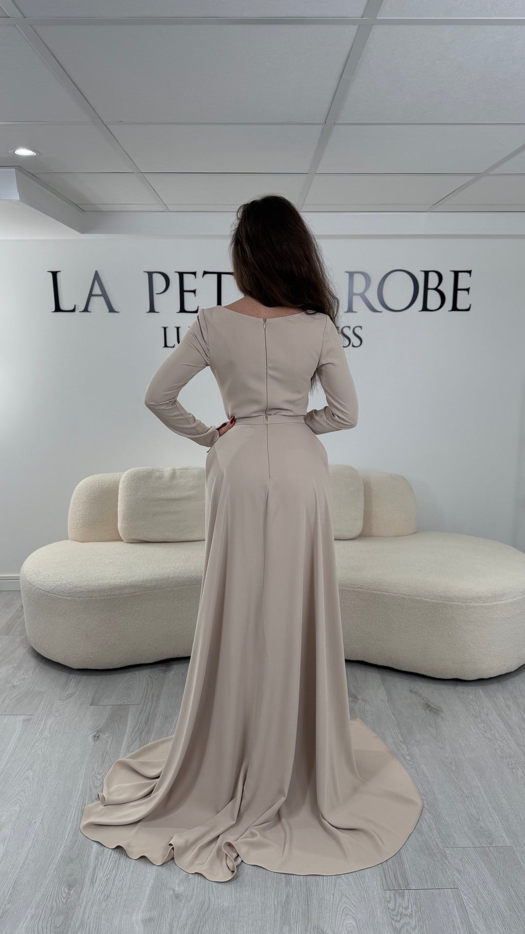 Robe de soirée beige avec col carré et manches longues. Coupe ajustée sans fente avec traîne amovible, idéale pour une allure élégante et raffinée.
