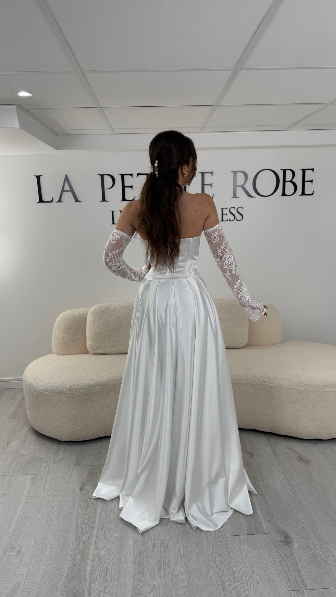 Robe de mariée blanche avec col bustier et manches amovibles en dentelle. Coupe fluide avec fente élégante, idéale pour une allure romantique et chic.