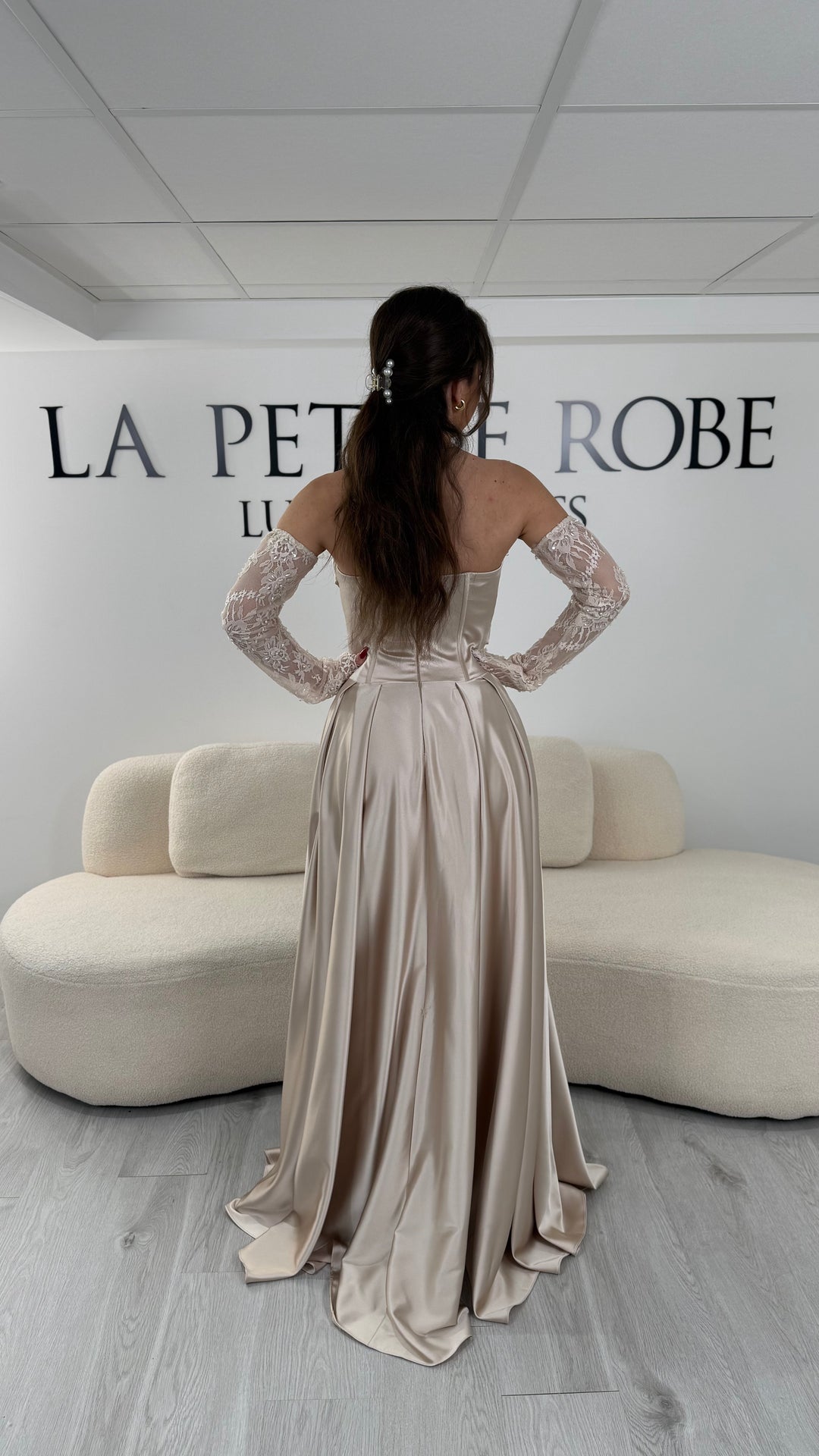 Robe de soirée beige avec col bustier et manches amovibles en dentelle. Coupe fluide avec fente élégante, idéale pour une allure chic et romantique.