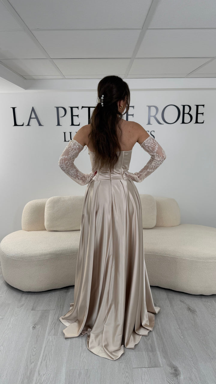 Robe de soirée beige avec col bustier et manches amovibles en dentelle. Coupe fluide avec fente élégante, idéale pour une allure chic et romantique.