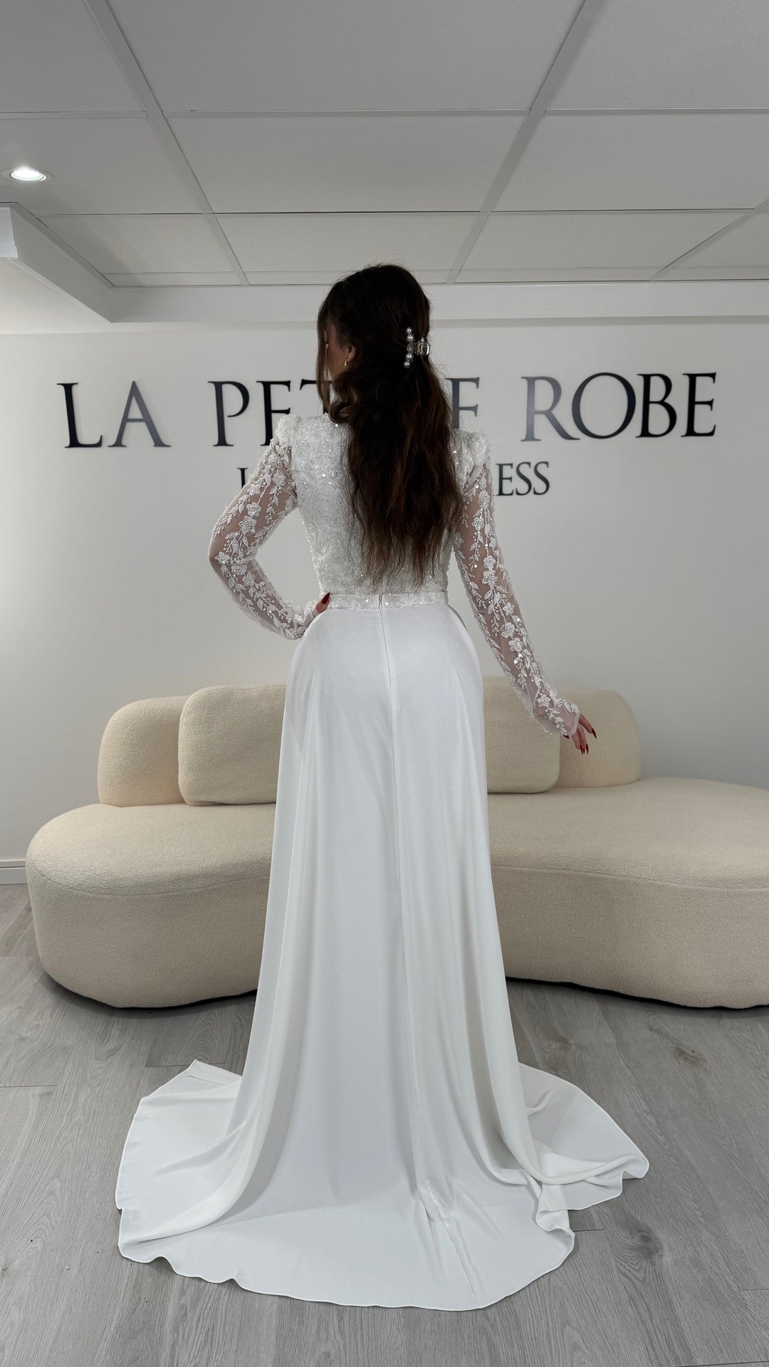 Robe de soirée blanche avec col carré et manches longues brodées. Coupe ajustée sans fente avec traîne amovible, idéale pour une allure élégante.