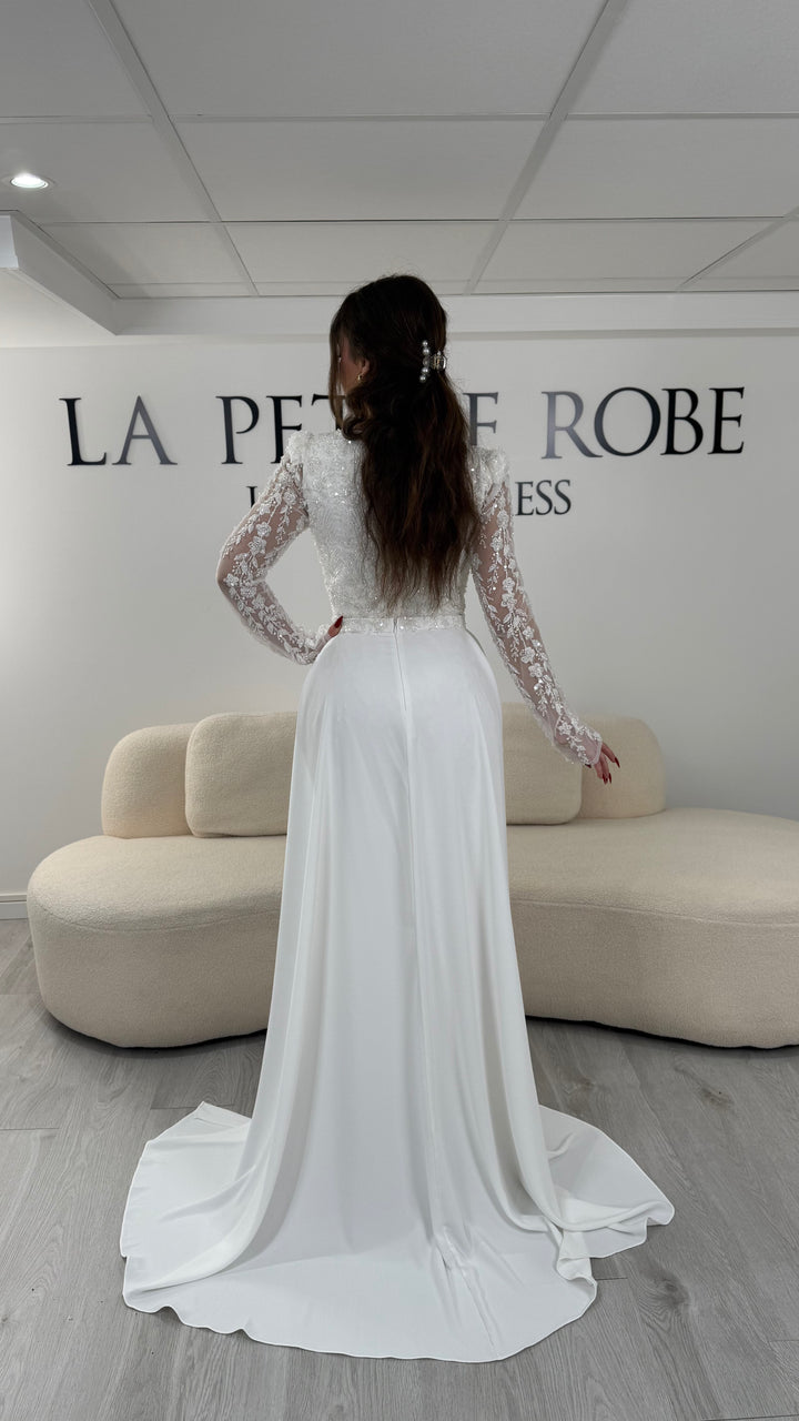 Robe de soirée blanche avec col carré et manches longues brodées. Coupe ajustée sans fente avec traîne amovible, idéale pour une allure élégante.