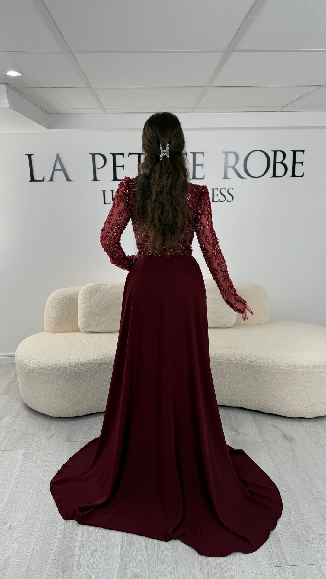Robe de soirée bordeaux avec col carré et manches longues brodées. Coupe ajustée sans fente avec traîne amovible, idéale pour une allure élégante.