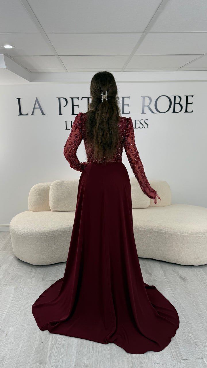 Robe de soirée bordeaux avec col carré et manches longues brodées. Coupe ajustée sans fente avec traîne amovible, idéale pour une allure élégante.
