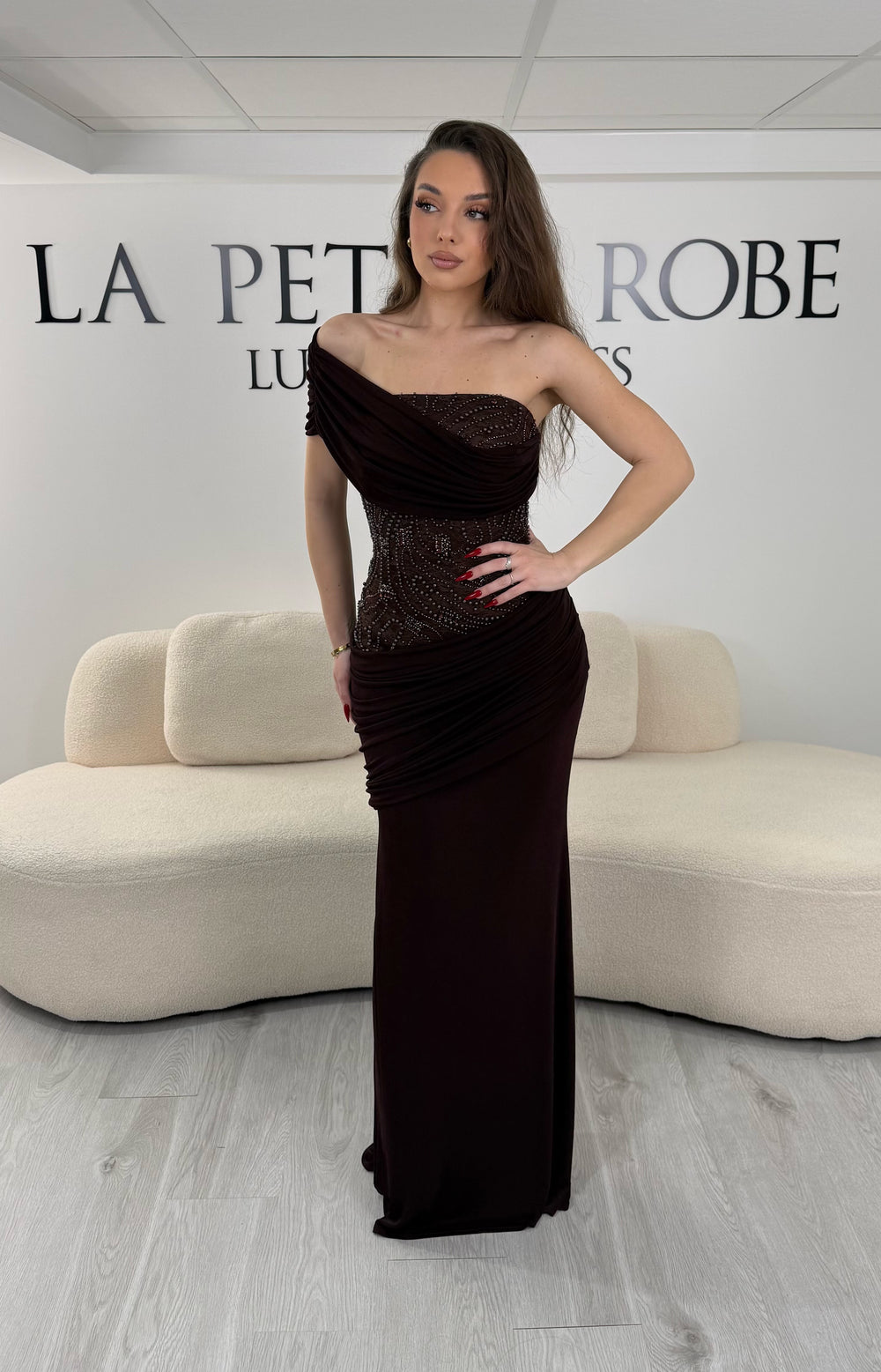 Robe de soirée marron en jersey stretch, sans manche avec col asymétrique. Coupe ajustée sans fente, idéale pour une allure élégante et moderne.