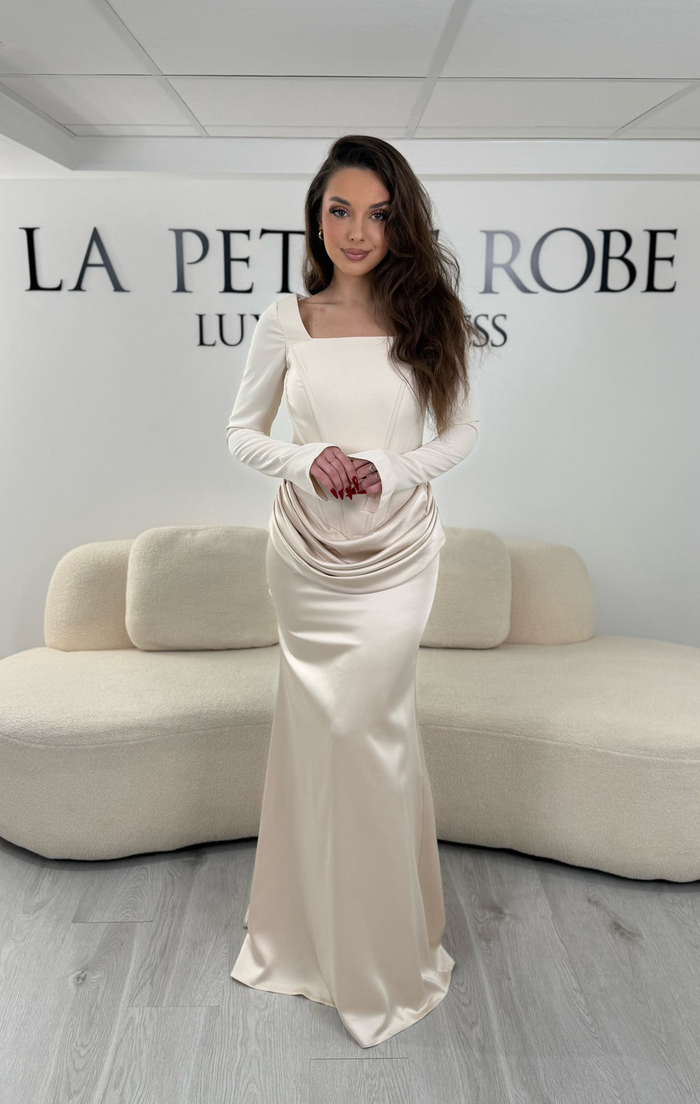 Robe de soirée beige avec col carré, manches longues et corset structuré. Coupe ajustée sans fente avec drapé élégant, idéale pour une allure chic.