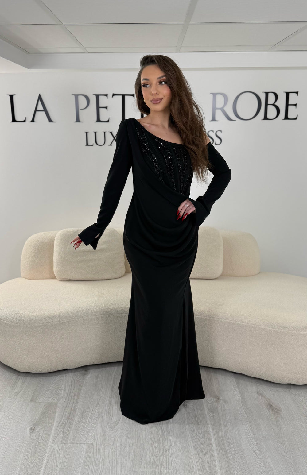 Robe de soirée noire avec col asymétrique et manches longues. Coupe ajustée avec fente sur le côté, idéale pour une allure élégante et sophistiquée.