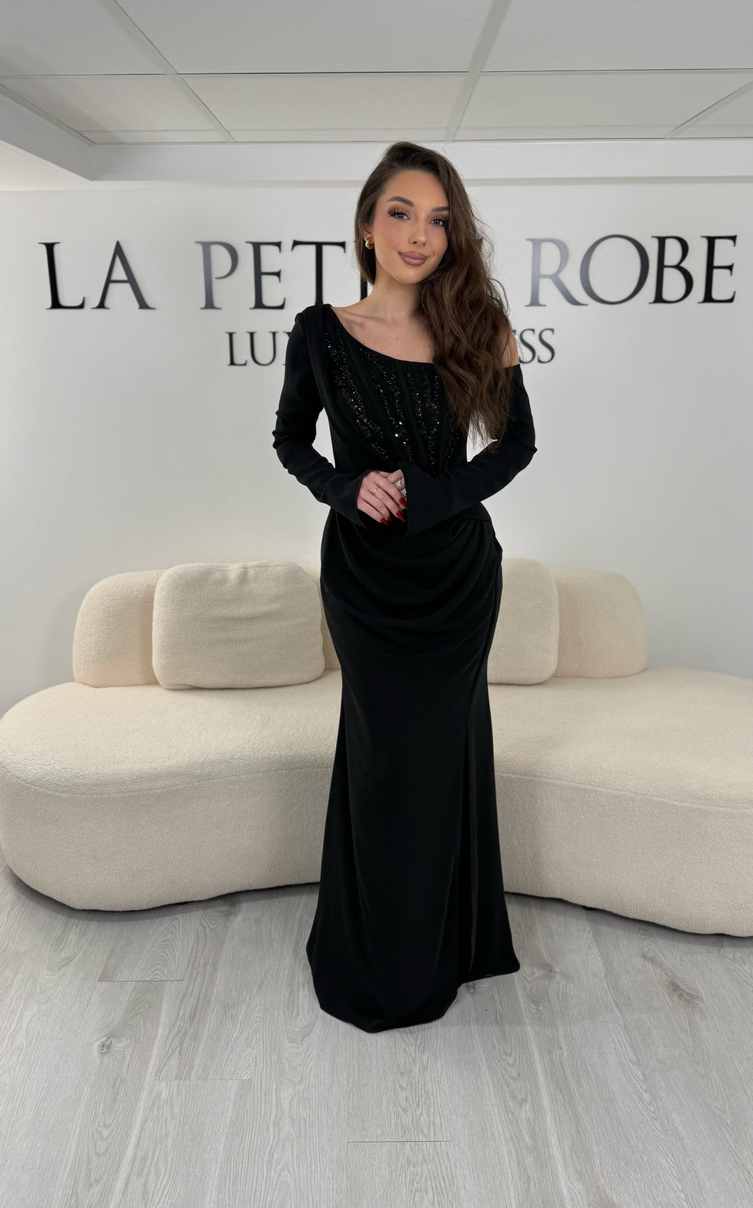 Robe de soirée noire avec col asymétrique et manches longues. Coupe ajustée avec fente sur le côté, idéale pour une allure élégante et sophistiquée.