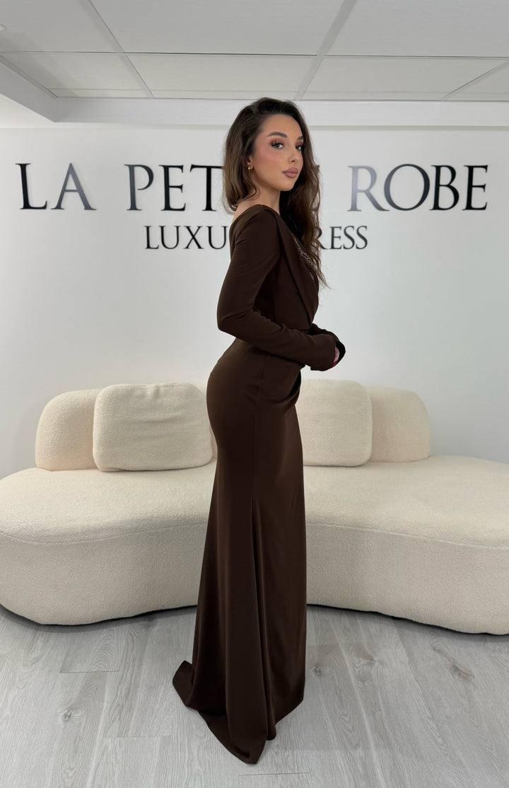 Robe de soirée marron avec col asymétrique et manches longues. Coupe ajustée avec fente sur le côté, idéale pour une allure élégante et sophistiquée.