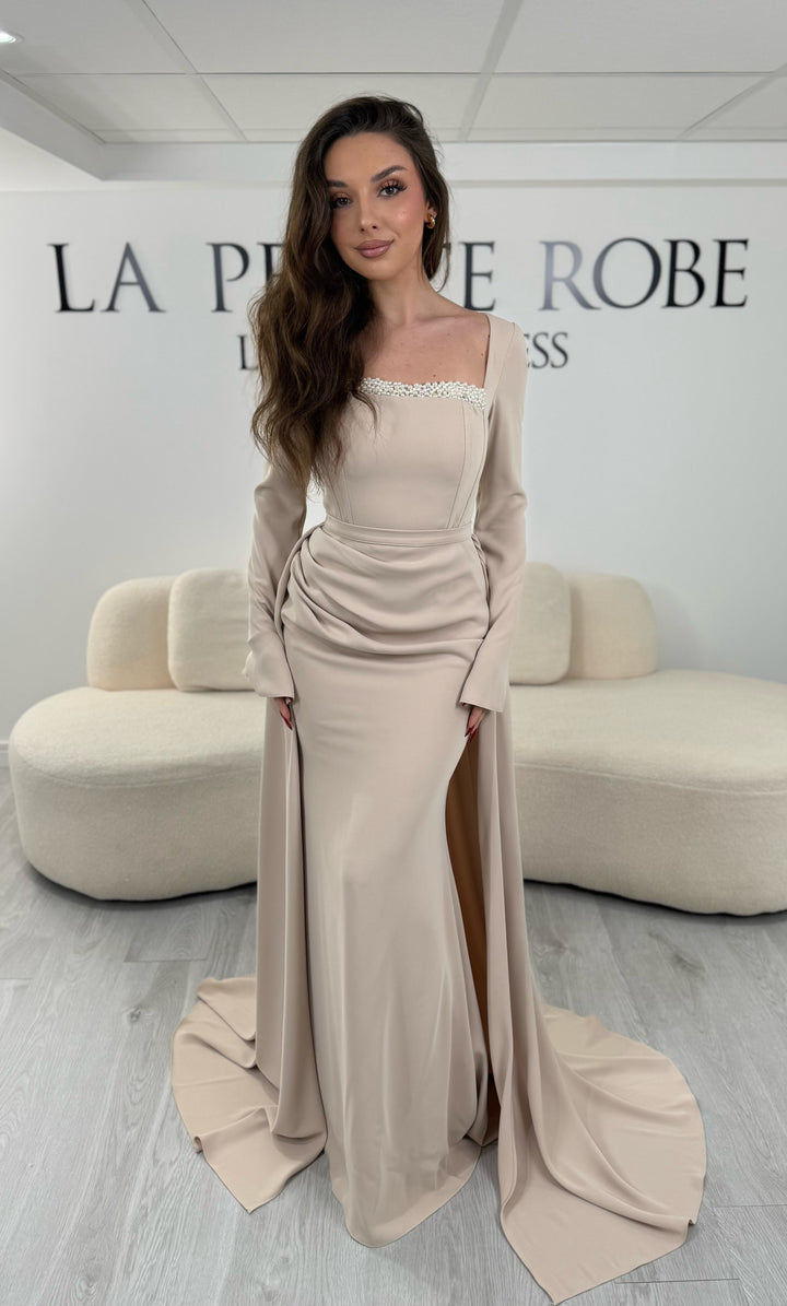 Robe de soirée beige avec col carré et manches longues. Coupe ajustée sans fente avec traîne amovible, idéale pour une allure élégante et raffinée.