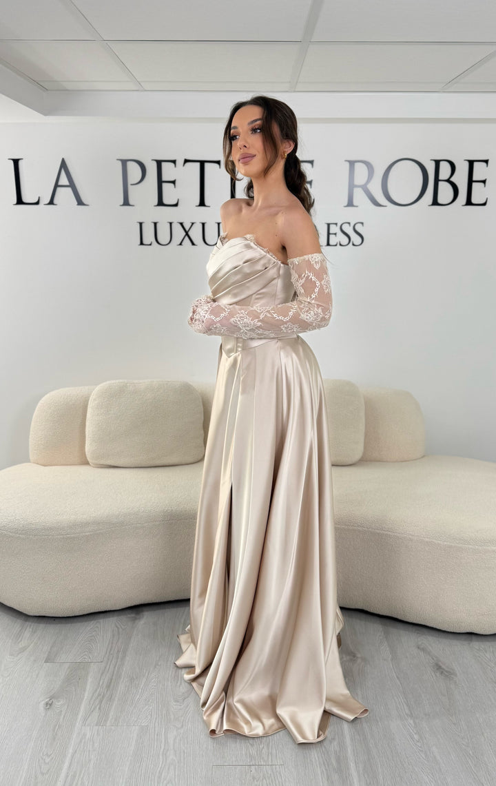 Robe de soirée beige avec col bustier et manches amovibles en dentelle. Coupe fluide avec fente élégante, idéale pour une allure chic et romantique.