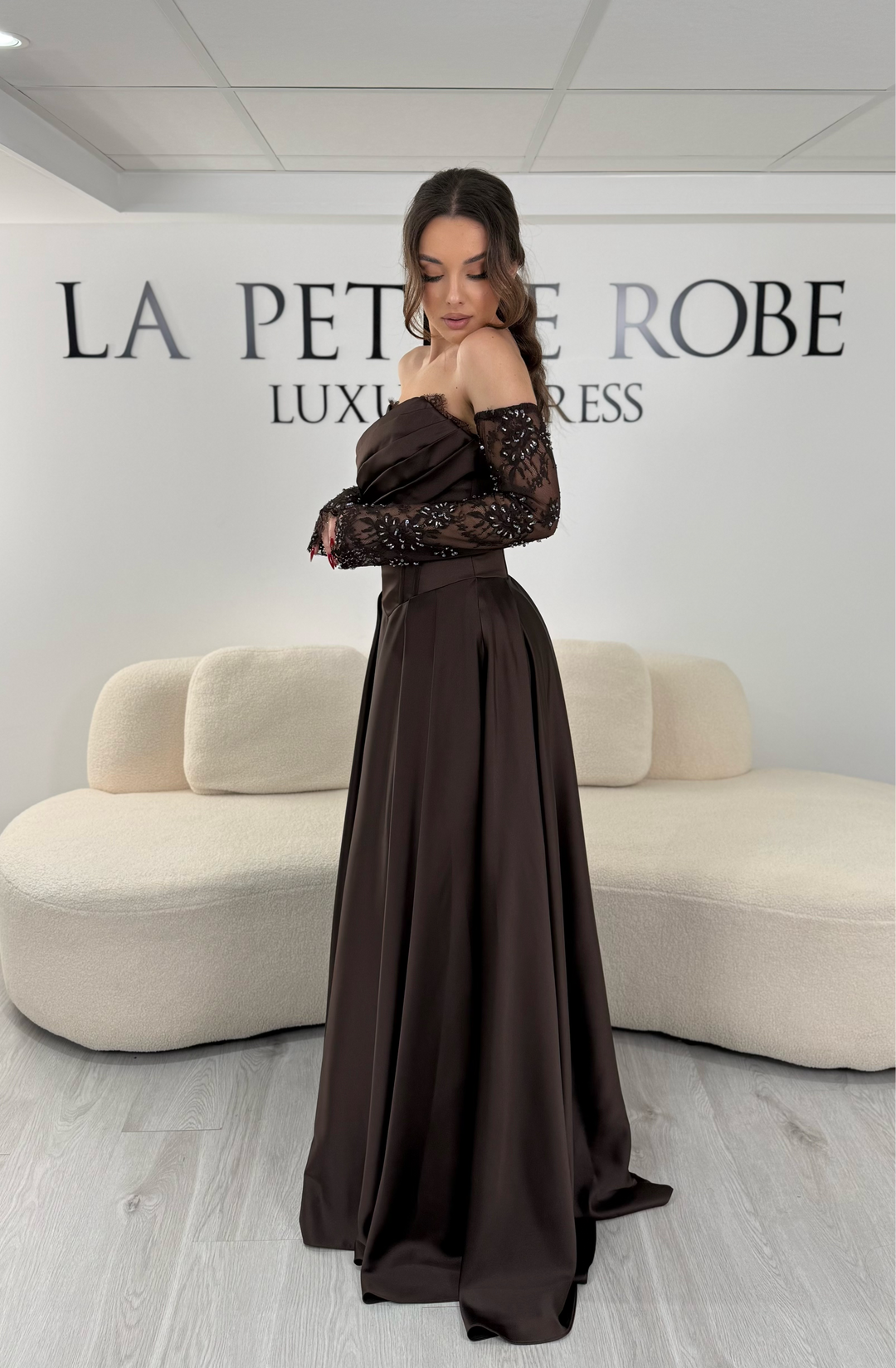 Robe de soirée marron avec col bustier et manches amovibles en dentelle. Coupe fluide avec fente élégante, idéale pour une allure chic et sophistiquée.