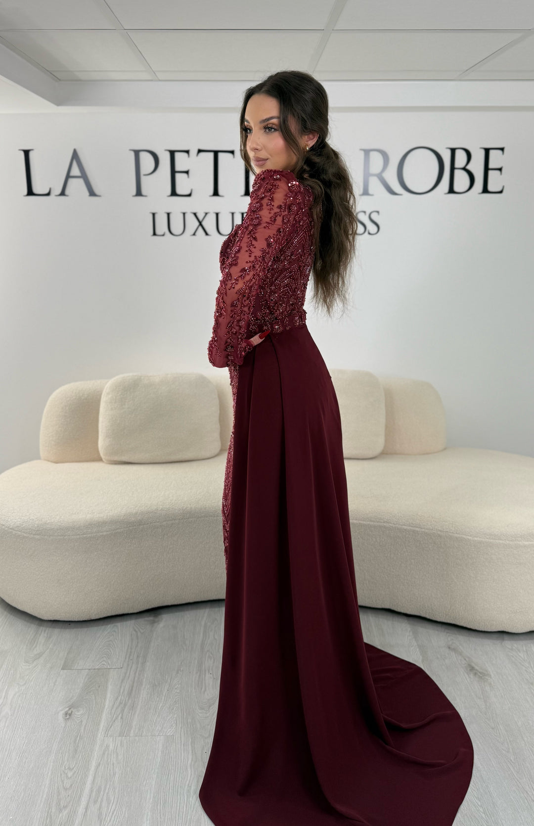 Robe de soirée bordeaux avec col carré et manches longues brodées. Coupe ajustée sans fente avec traîne amovible, idéale pour une allure élégante.