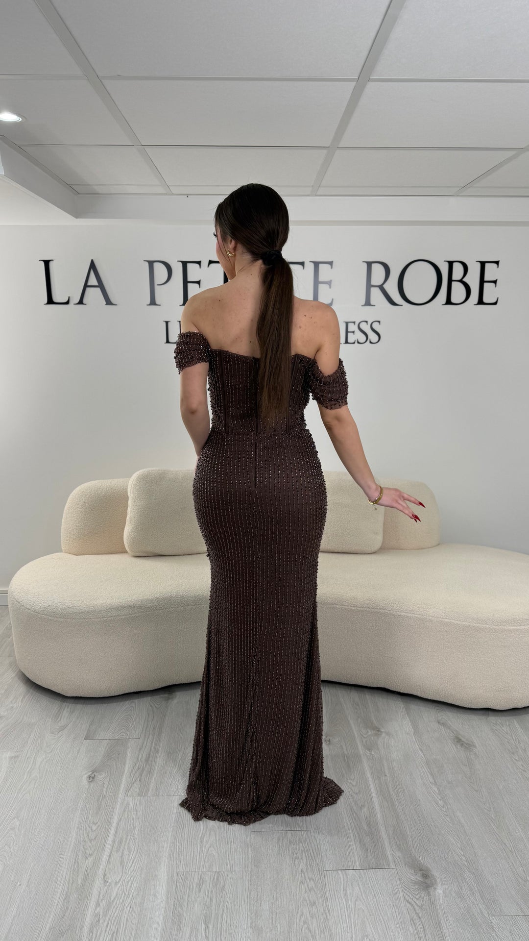 Robe de soirée marron avec col bateau et design sans manche. Coupe ajustée sans fente, ornée de perles pour une allure élégante et glamour.