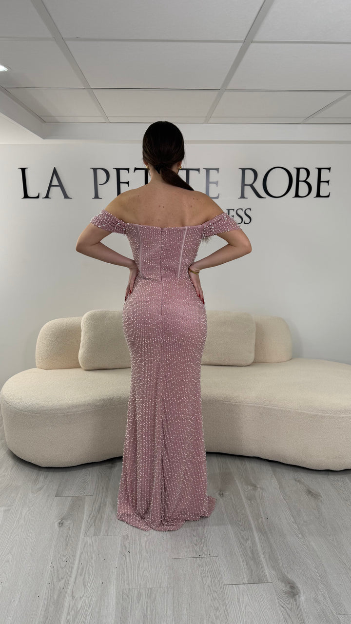 Robe de soirée rose avec col bateau et design sans manche. Coupe ajustée sans fente, ornée de perles pour une allure élégante et glamour.