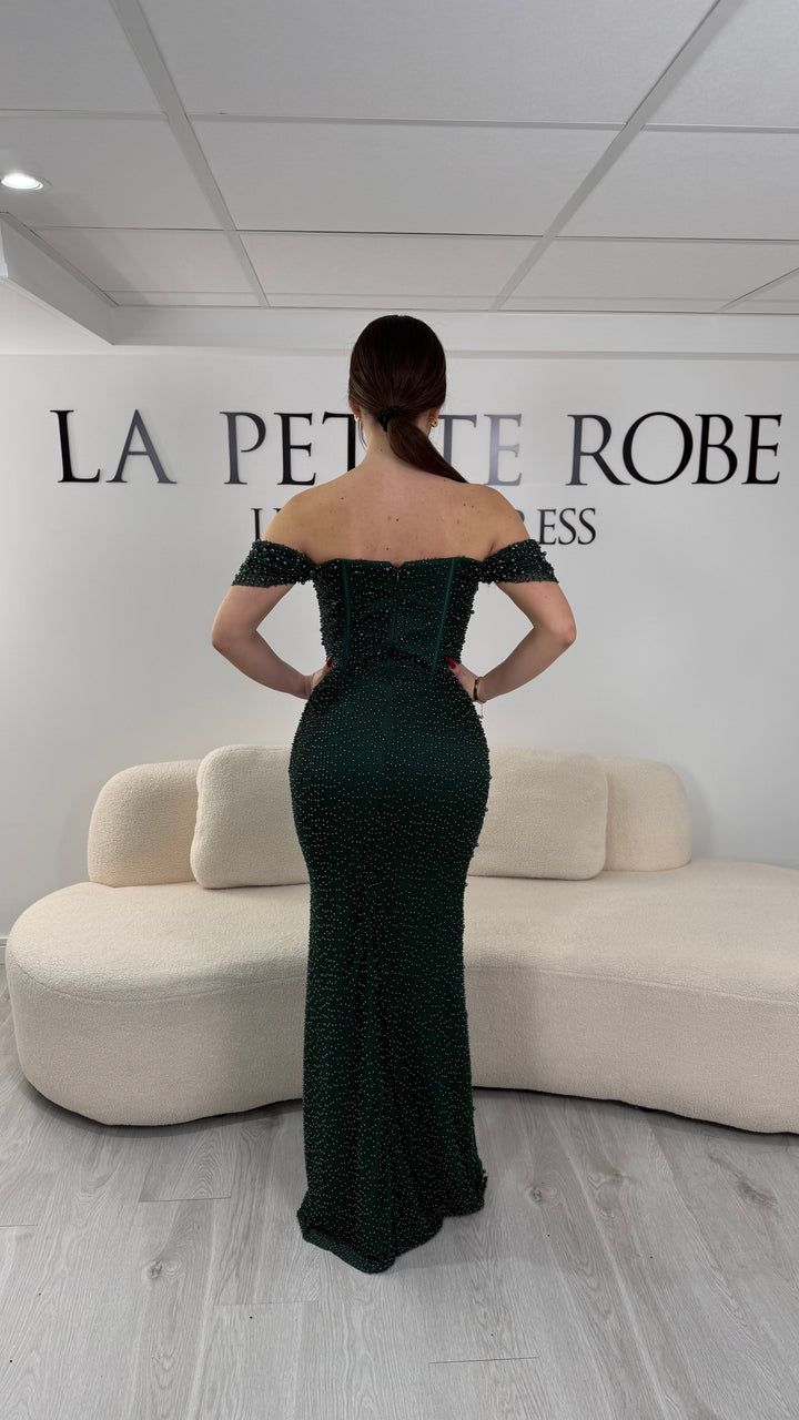 Robe de soirée vert émeraude avec col bateau et design sans manche. Coupe ajustée sans fente, ornée de perles pour une allure élégante et glamour.