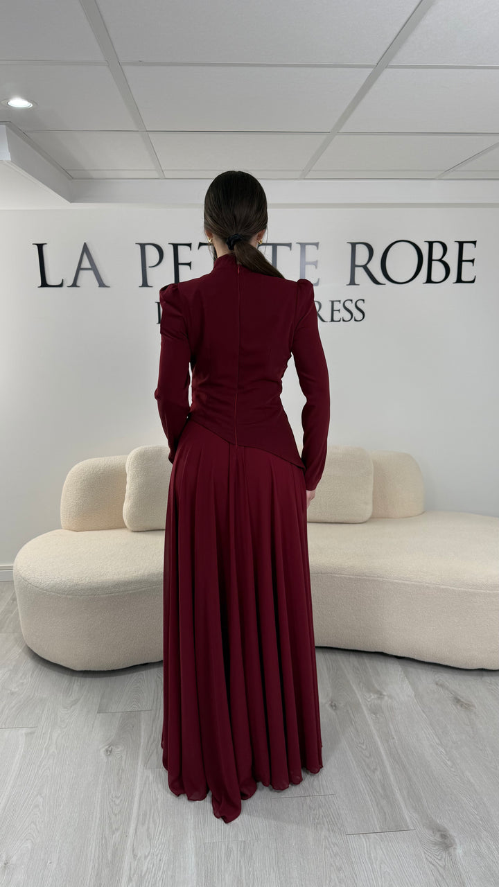 Robe de soirée bordeaux avec manches longues et col montant. Coupe fluide sans fente, idéale pour une allure élégante et sophistiquée.