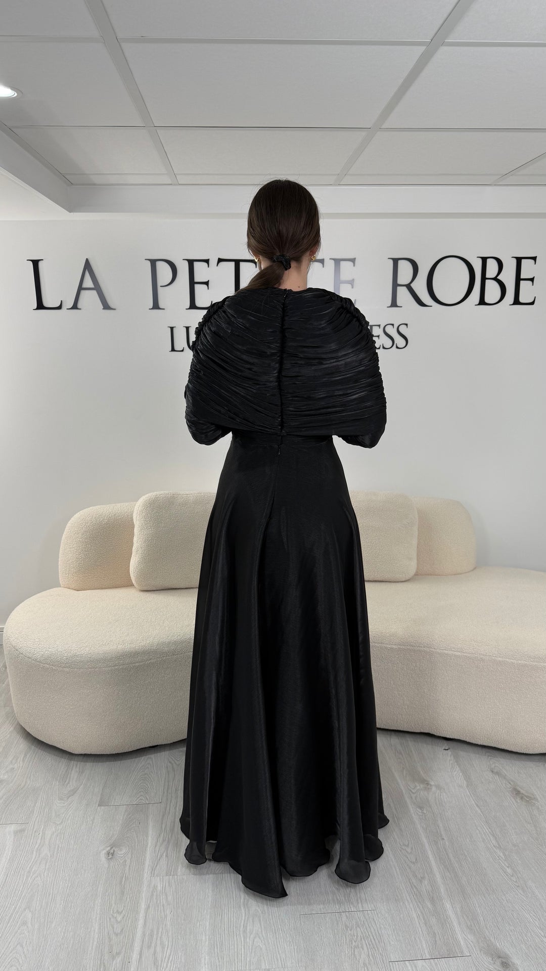 Robe de soirée modeste noire avec manches longues et drapé élégant. Coupe fluide sans fente, idéale pour une allure chic et raffinée.