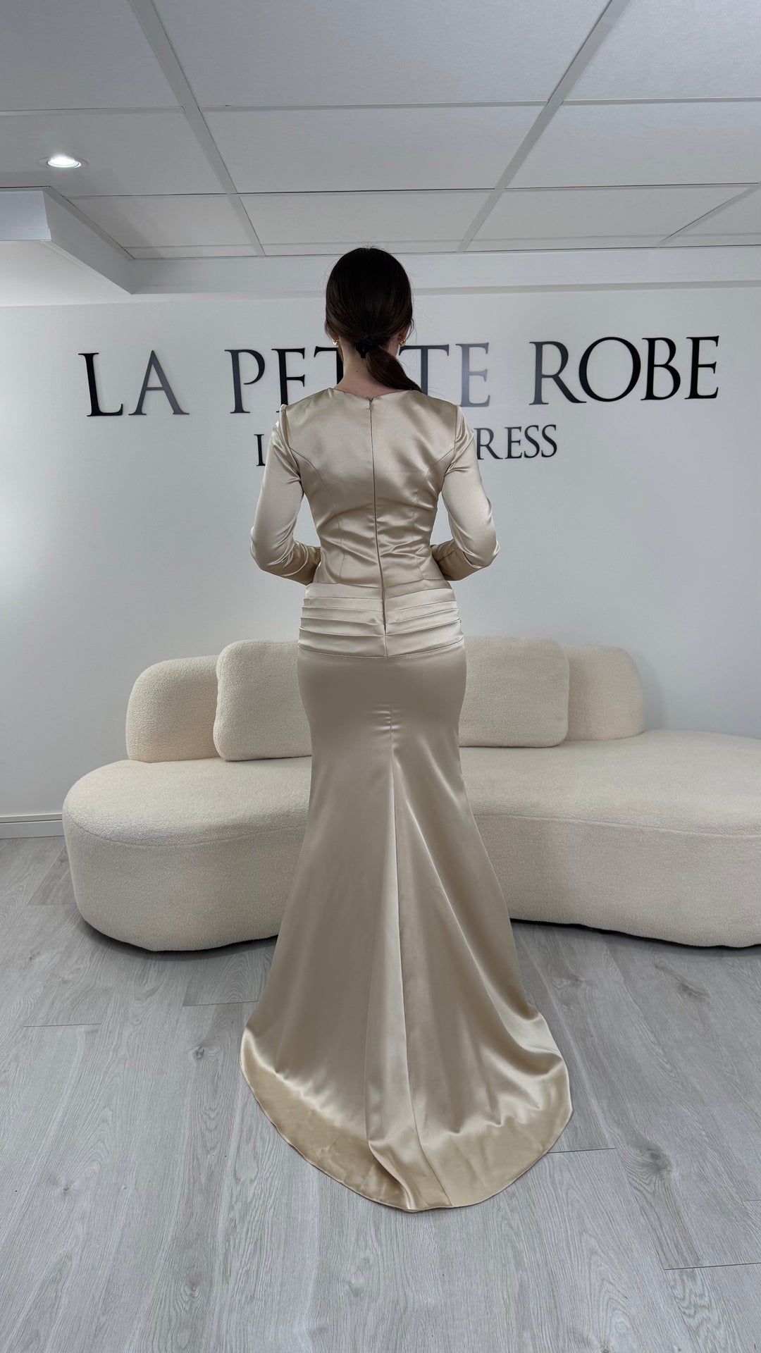 Robe de soirée beige avec manches longues et coupe ajustée. Sans fente, tissu satiné et détails élégants pour une allure sophistiquée.