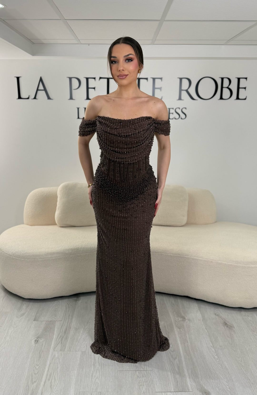 Robe de soirée marron avec col bateau et design sans manche. Coupe ajustée sans fente, ornée de perles pour une allure élégante et glamour.