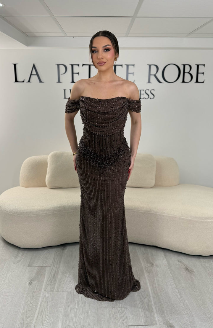 Robe de soirée marron avec col bateau et design sans manche. Coupe ajustée sans fente, ornée de perles pour une allure élégante et glamour.