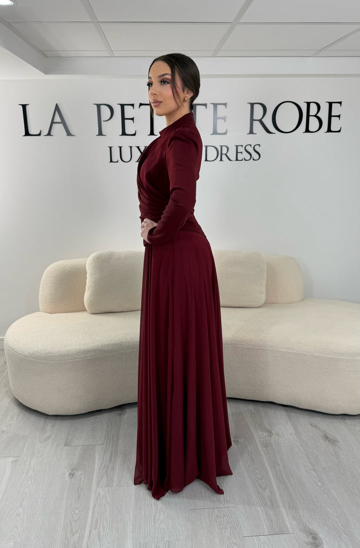 Robe de soirée bordeaux avec manches longues et col montant. Coupe fluide sans fente, idéale pour une allure élégante et sophistiquée.