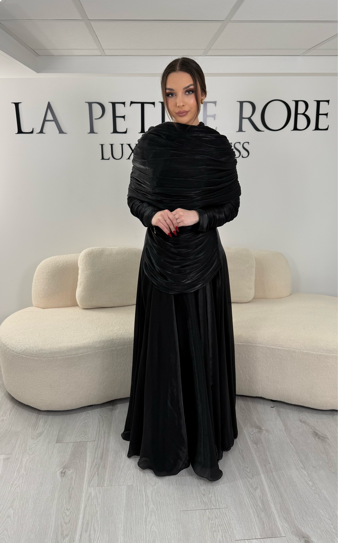 Robe de soirée modeste noire avec manches longues et drapé élégant. Coupe fluide sans fente, idéale pour une allure chic et raffinée.