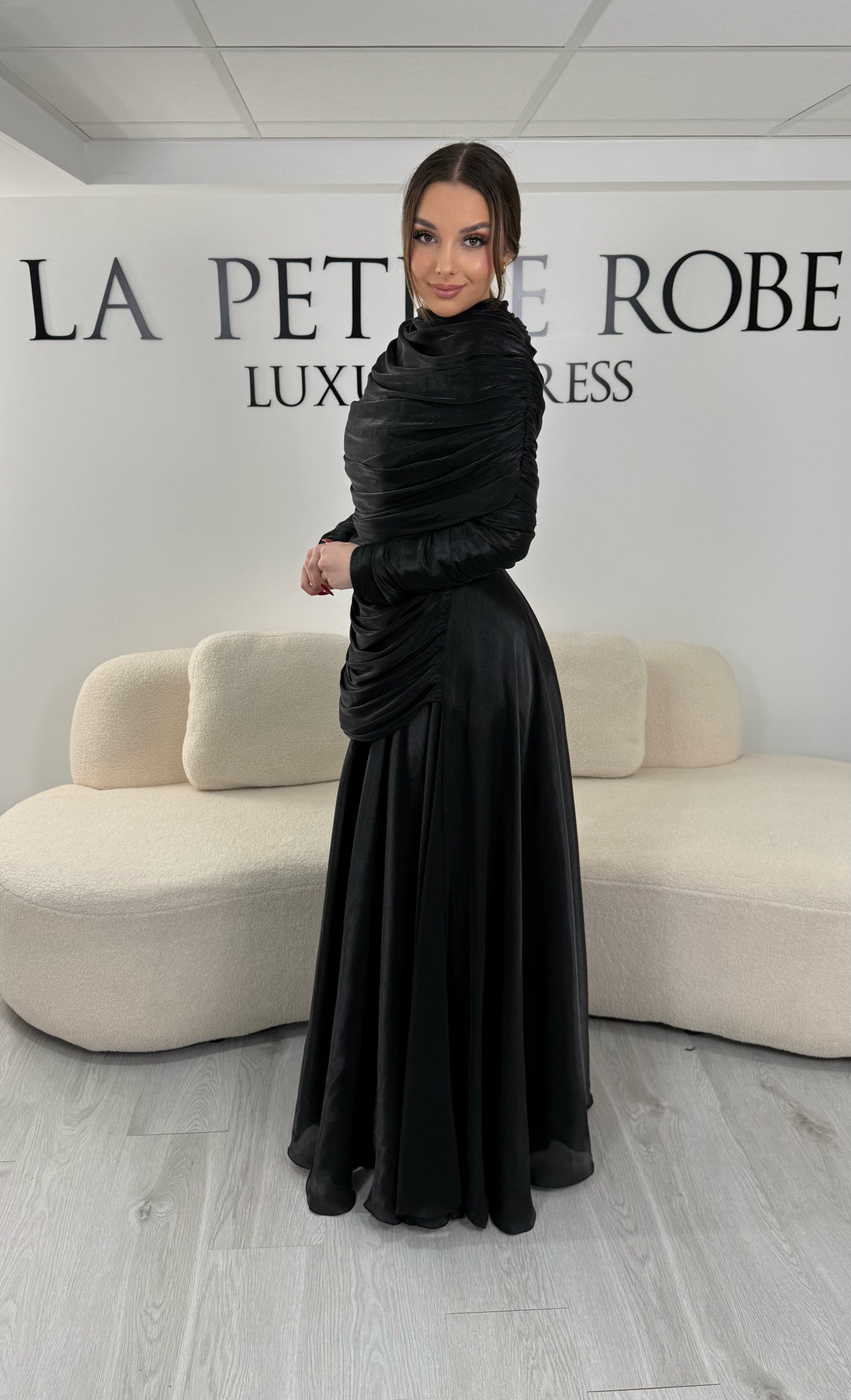Robe de soirée modeste noire avec manches longues et drapé élégant. Coupe fluide sans fente, idéale pour une allure chic et raffinée.