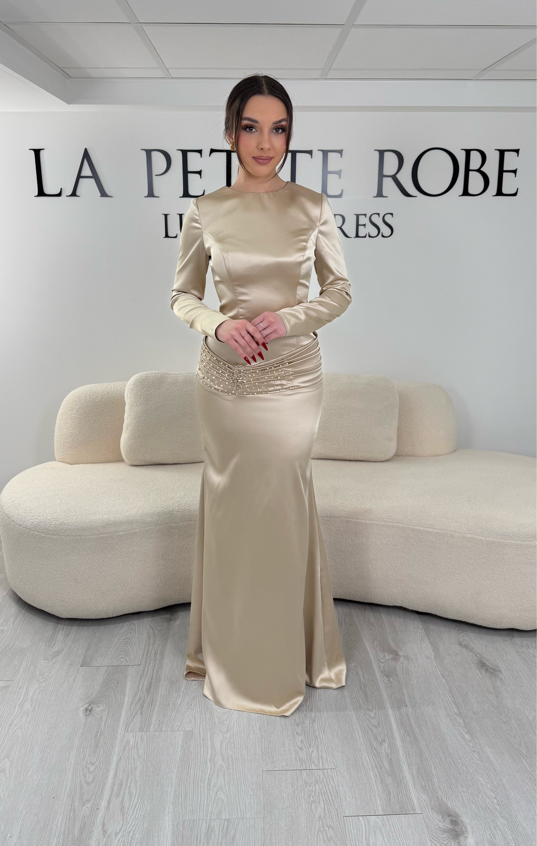 Robe de soirée beige avec manches longues et coupe ajustée. Sans fente, tissu satiné et détails élégants pour une allure sophistiquée.