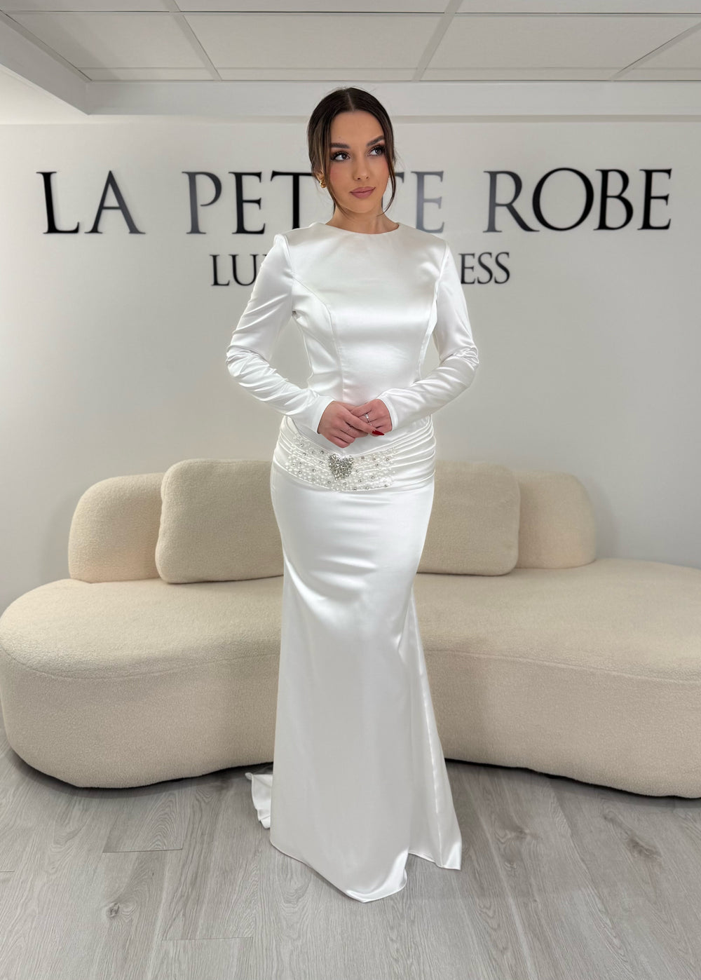 Robe de mariée blanche avec manches longues et coupe ajustée. Sans fente, tissu satiné et détails élégants pour une allure raffinée et intemporelle.