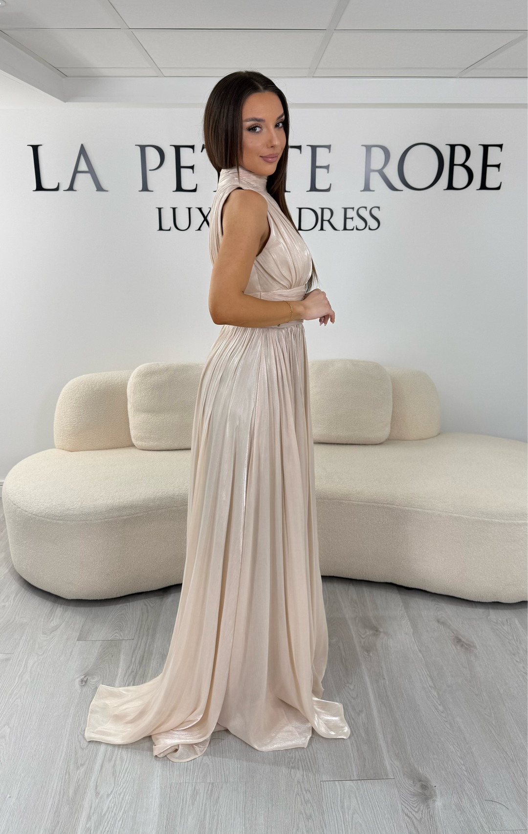 Robe de soirée beige longue plissée avec col montant et coupe sans manches. Une robe élégante sans fente idéale pour mariage, cérémonie et soirée chic.