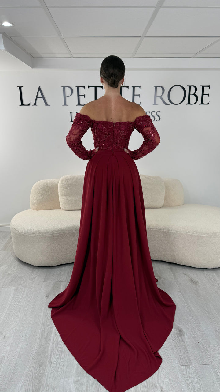 Robe de soirée bordeaux longue avec dentelle raffinée, manches longues et décolleté bardot. Modèle élégant sans fente avec traîne amovible, idéal pour mariage et cérémonie.