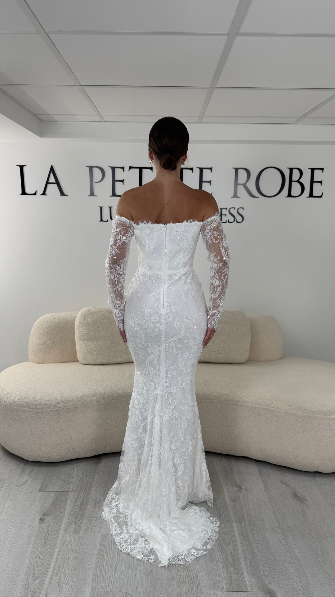 Robe de mariée blanche longue en dentelle et sequins avec col bardot et manches longues. Une robe élégante sans fente idéale pour cérémonie, mariage civil et réception.