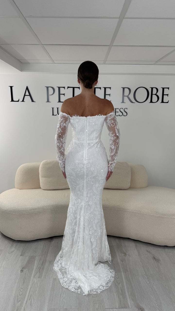 Robe de mariée blanche longue en dentelle et sequins avec col bardot et manches longues. Une robe élégante sans fente idéale pour cérémonie, mariage civil et réception.