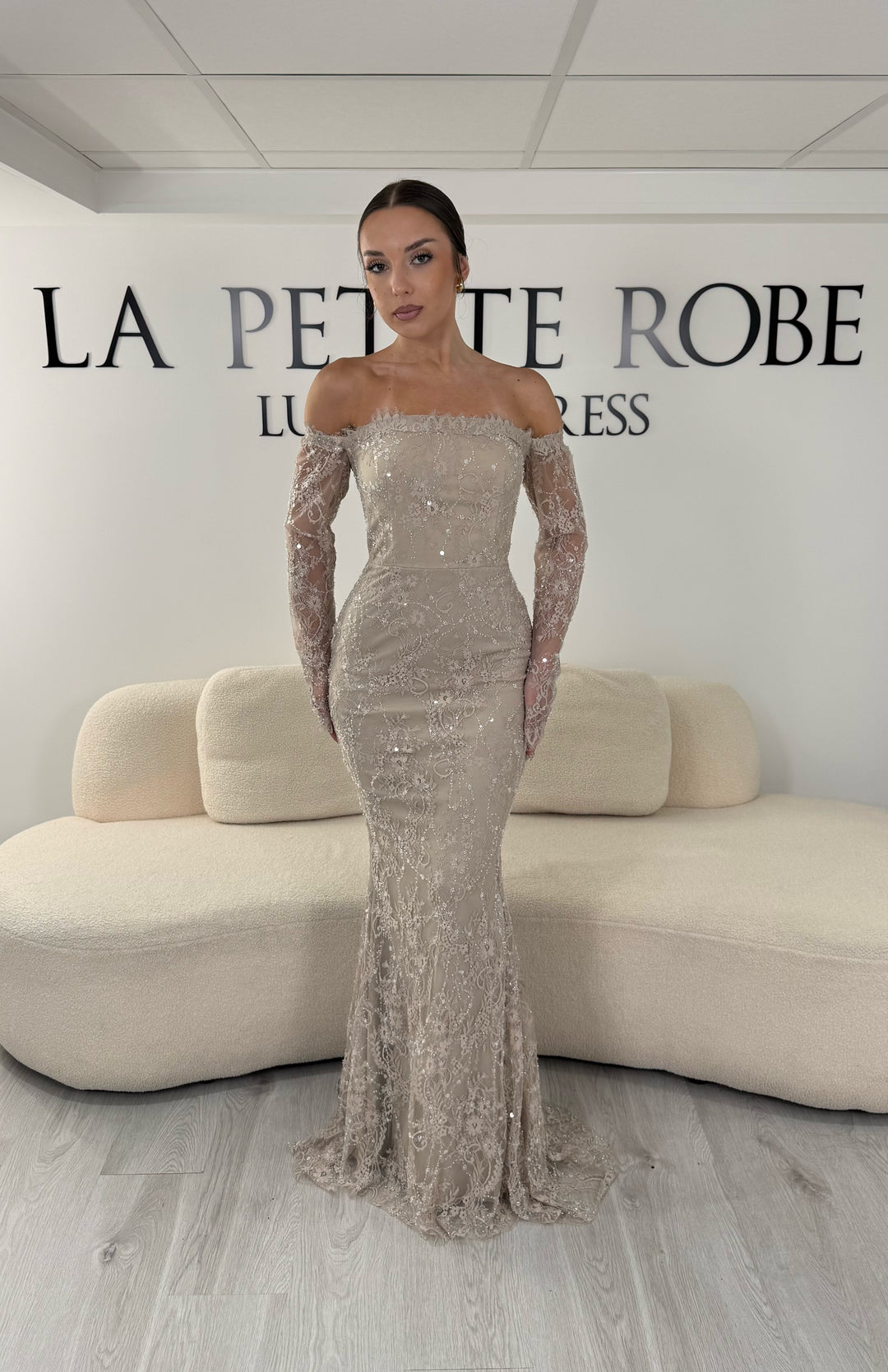 Robe de soirée taupe longue en dentelle et sequins avec col bardot et manches longues. Une robe élégante sans fente idéale pour mariage, gala et cérémonie.
