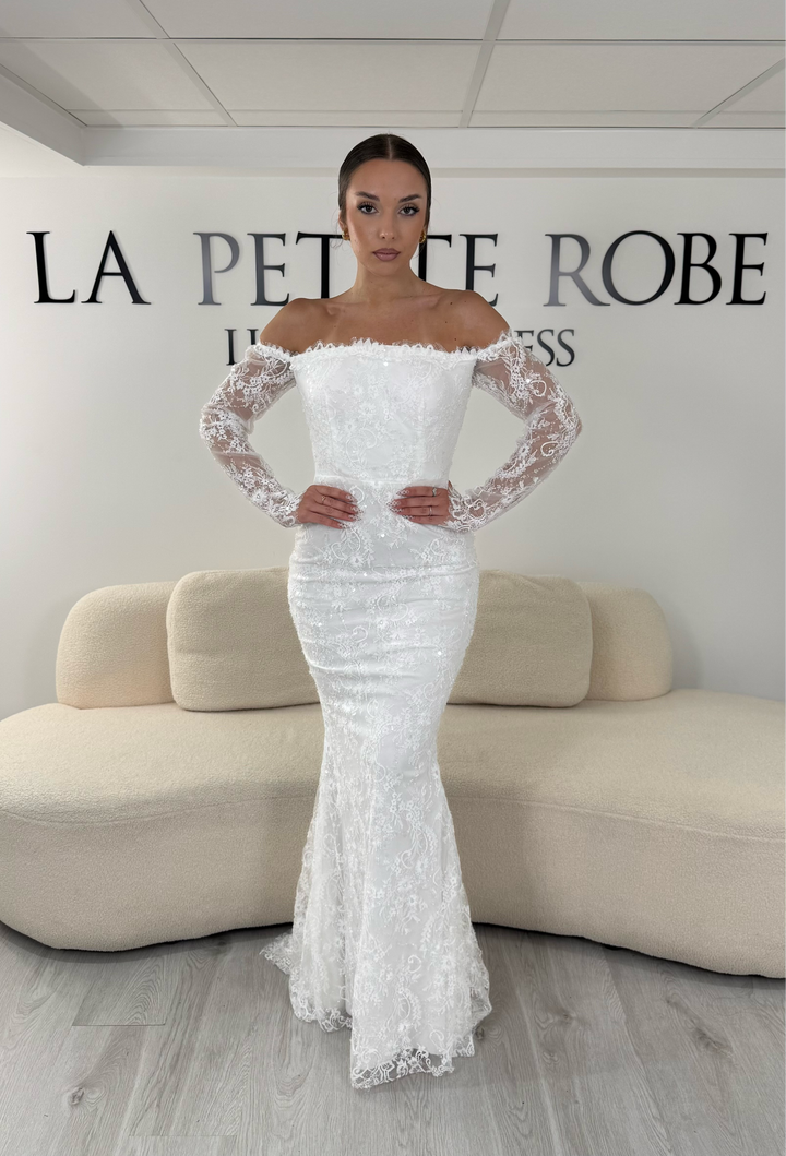 Robe de mariée blanche longue en dentelle et sequins avec col bardot et manches longues. Une robe élégante sans fente idéale pour cérémonie, mariage civil et réception.