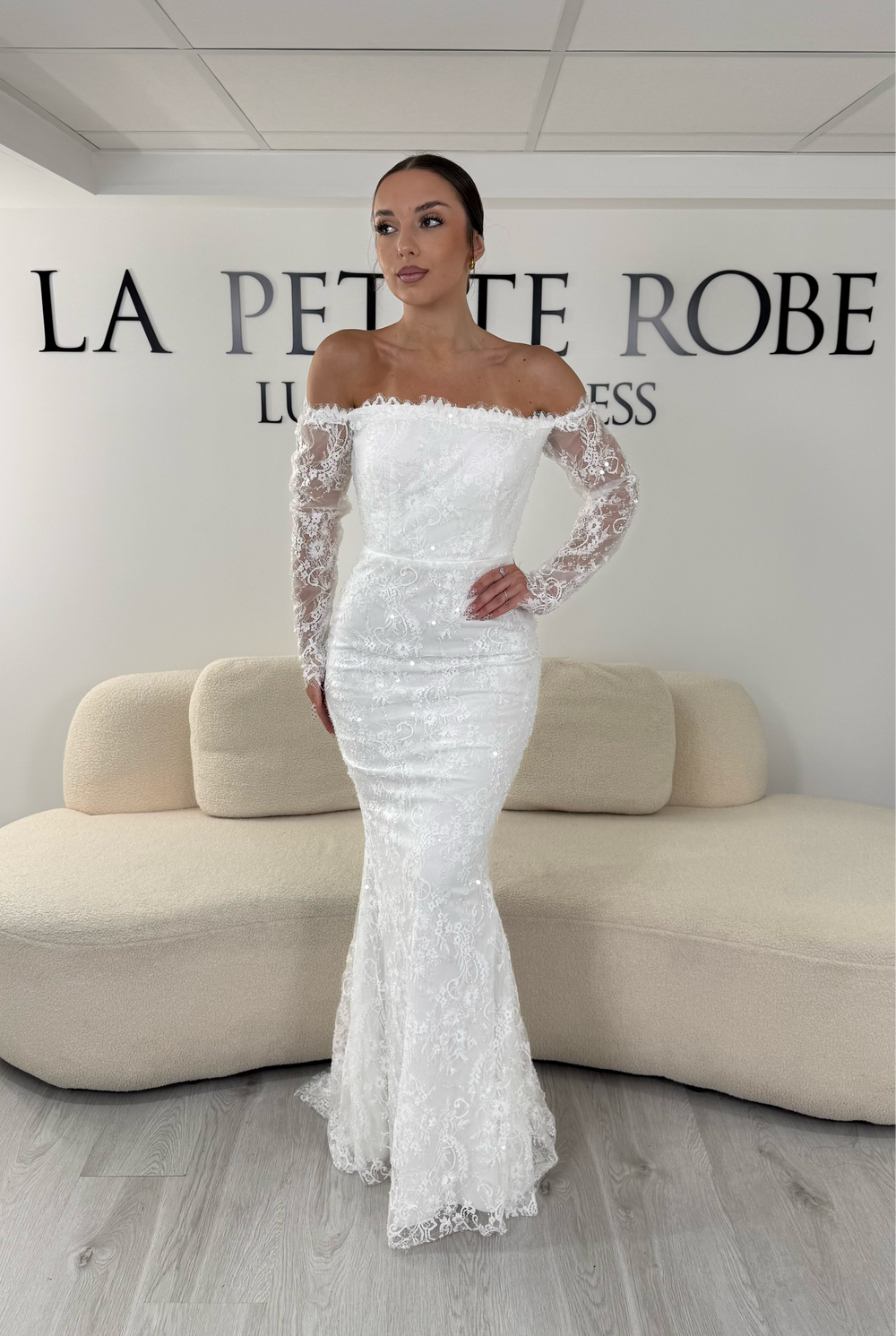 Robe de mariée blanche longue en dentelle et sequins avec col bardot et manches longues. Une robe élégante sans fente idéale pour cérémonie, mariage civil et réception.