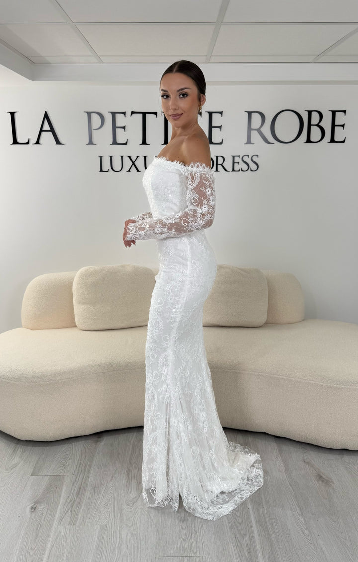 Robe de mariée blanche longue en dentelle et sequins avec col bardot et manches longues. Une robe élégante sans fente idéale pour cérémonie, mariage civil et réception.