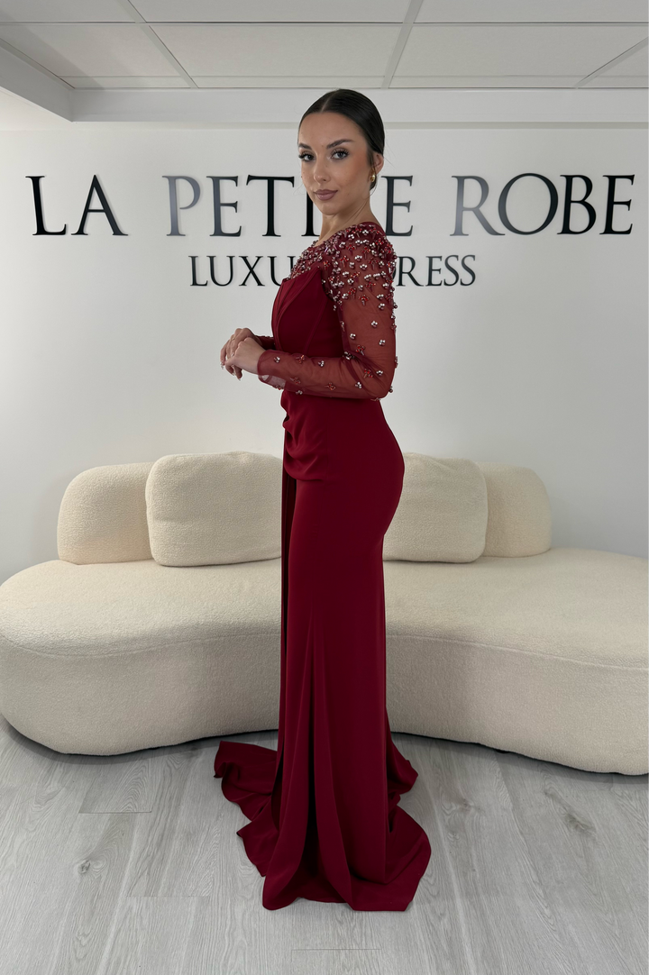 Robe de soirée bordeaux longue avec col rond, manches longues brodées et détails perlés. Une robe élégante avec fente, idéale pour mariage, gala et cérémonie.
