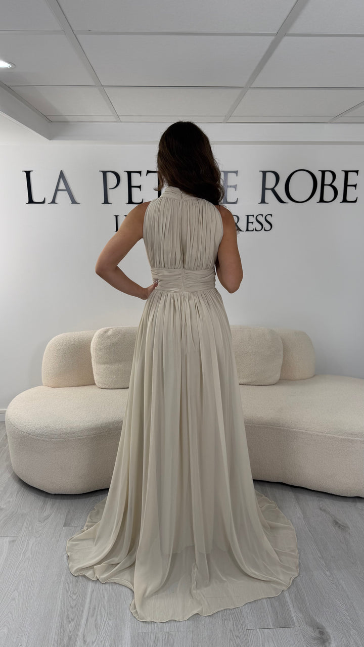 Découvrez cette robe de soirée beige longue et fluide. Sans manche, avec col montant drapé et sans fente, elle offre une allure élégante et raffinée pour toutes vos occasions.
