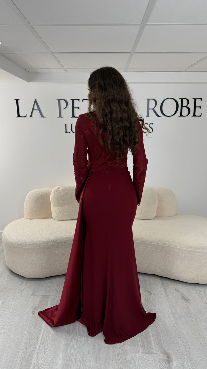Découvrez cette robe de soirée bordeaux avec col rond, manches longues en dentelle et élégante traîne sur le côté. Une robe sans fente, parfaite pour une allure raffinée.