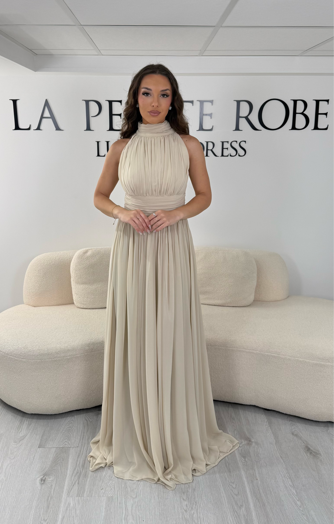 Découvrez cette robe de soirée beige longue et fluide. Sans manche, avec col montant drapé et sans fente, elle offre une allure élégante et raffinée pour toutes vos occasions.